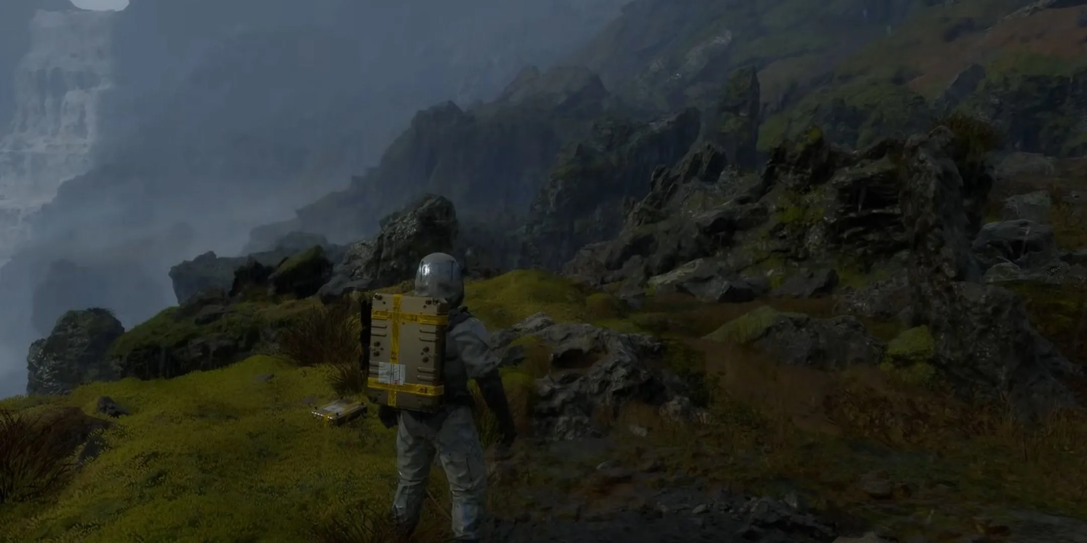 Sam Porter Bridges vượt địa hình đồi núi hiểm trở trong Death Stranding bằng chân.